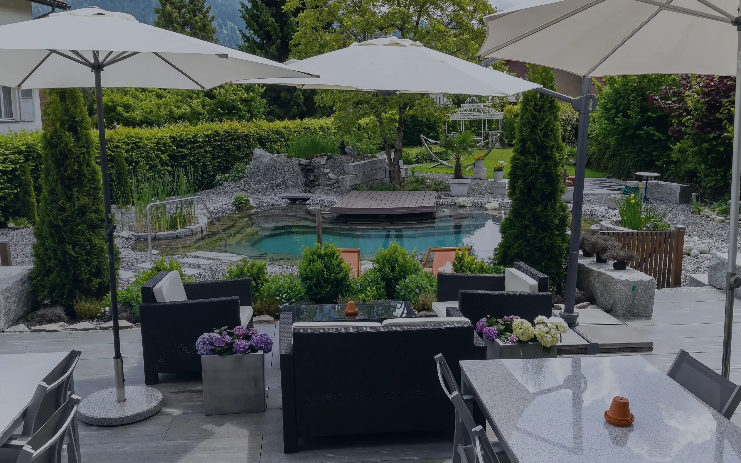Lounge im Hotelpark unter Sonnenschirmen, dahinter der Naturbadeteich