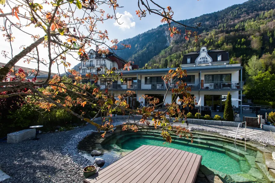 Hotelpark mit Naturbadeteich im Herbstlicht, dahinter der Annex und die Berge